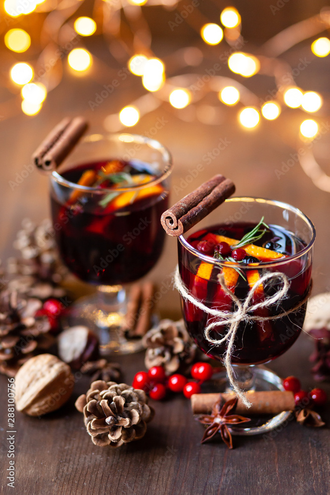 Composition with two glasses of hot mulled red wine with spices. Holiday atmosphere, christmas ligths on dark background. Rustic style, cones, nuts, anise, cinnamon, orang, berries as festive decor Composition with two glasses of hot mulled red wine with spices. Holiday atmosphere, christmas ligths on dark background. Rustic style, cones, nuts, anise, cinnamon, orang, berries as festive decor