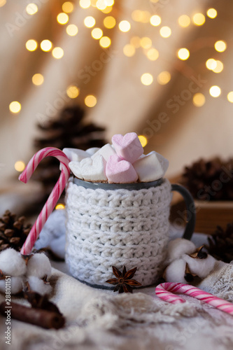 Holiday christmas composition with mug in knitted white sweater with strong hot coffee and marshmallows. Rustic decor, cotton, cones, cinnamon, anise. Lights on. Cozy quite romantic atmosphere