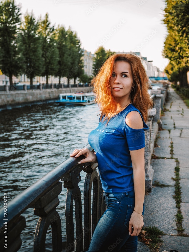 Brunette girl with long hair enjoys the evening sun on the river embankment in St. Petersburg