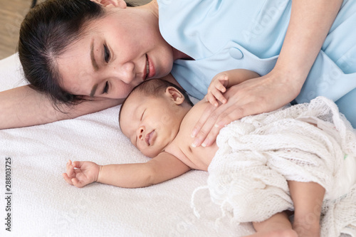 Asian beautiful mother hug adorable newborn baby 0-1 month sleep with comfortable safe in bed together at home