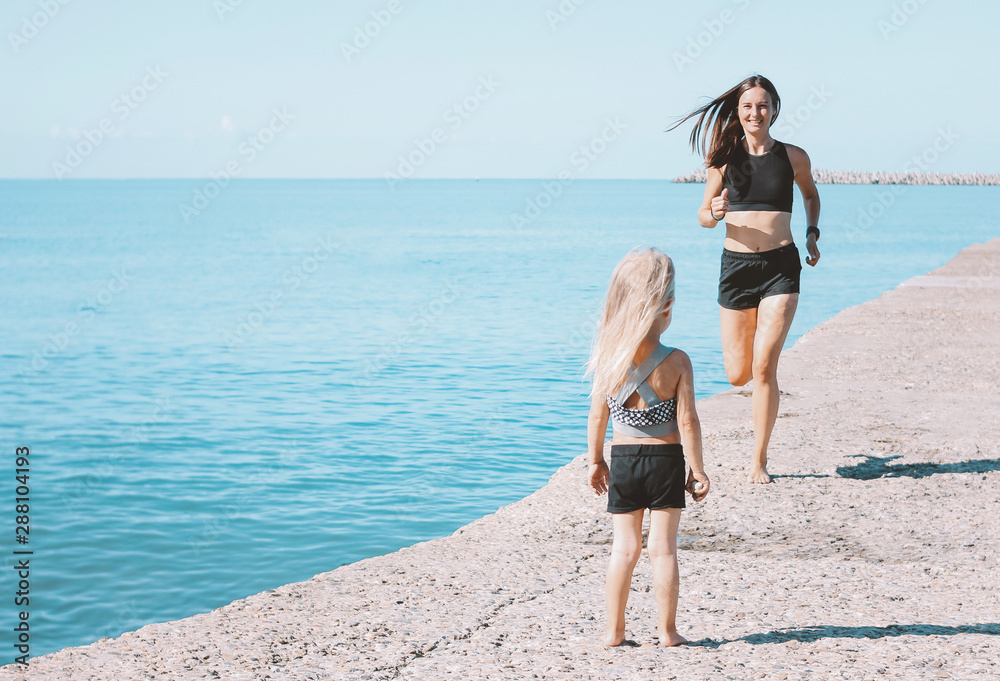 Little cute girl looking to fit mom running on the beach, healthy lifestyle, sport family