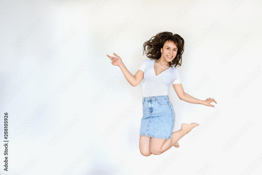 close up photo of a happy brunette in white blouse and denim skirt jumping in the air