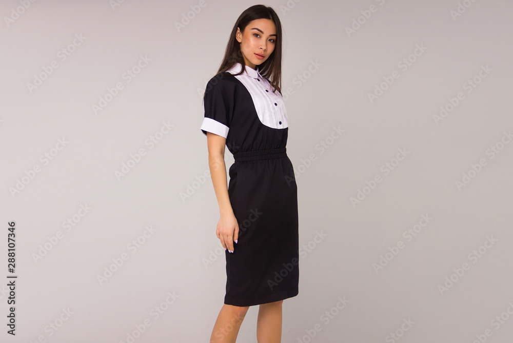 young stylish nurse with long brunette hair in black medical dress is standing in profile, looking straight and smiling on the gray wall background. medical fashion concept, free space young stylish nurse with long brunette hair in black medical dress is standing in profile, looking straight and smiling on the gray wall background. medical fashion concept, free space
