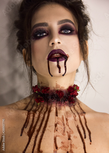 young brunette girl with stylish dark make-up with the blood that flows from her neck and mouth, halloween concept