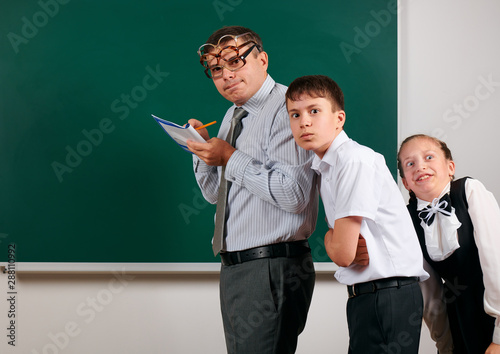 Portrait of a teacher checking homework, reading school exercise books, schoolboy and schoolgirl with old fashioned eyeglasses posing on blackboard background - back to school and education concept photo