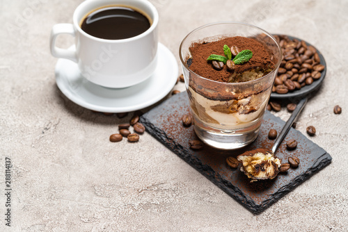 Portion of Classic tiramisu dessert in a glass cup on stone serving board and fres espresso coffee on concrete background photo