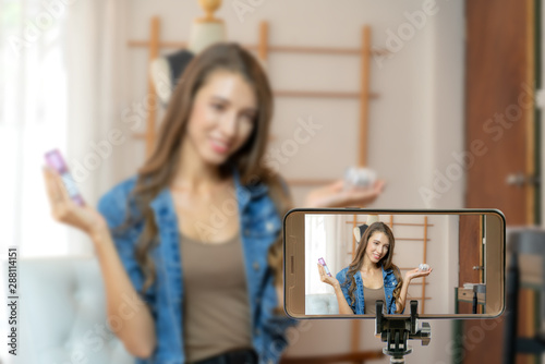 Beautiful asian woman blogger showing clothes in front of camera to recording vlog video live streaming at her shop.Business online influencer on social media concept