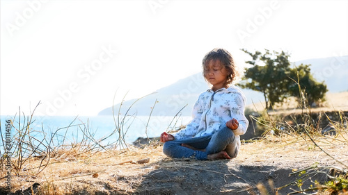 Cute little child gurl meditating alone in lotus pose at lake shore in windy weather © alexeg84