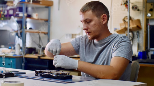 Electronic engineer of computer technology at work. Repairman repairs computer graphics card chipset in workshop. He is unscrewing the bolts sits at table. PC repair technician and electronic devices. photo