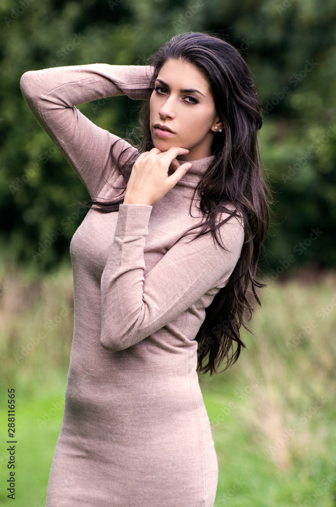 Portrait of fashionable woman with light brown sweater, posing outdoors. Fashion autumn photo. Woman brown long hair. Hand on face. Serious expression.