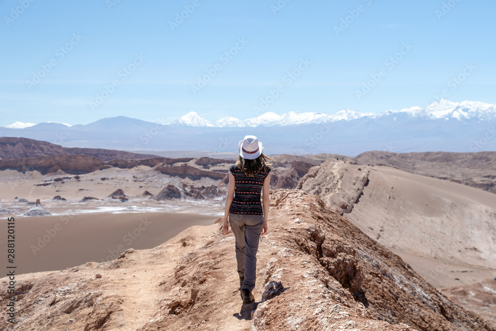 Young female solo traveler walking in hiking trail at Atacama Desert. Single Blond Caucasian girl explore Moon Valley in Chile