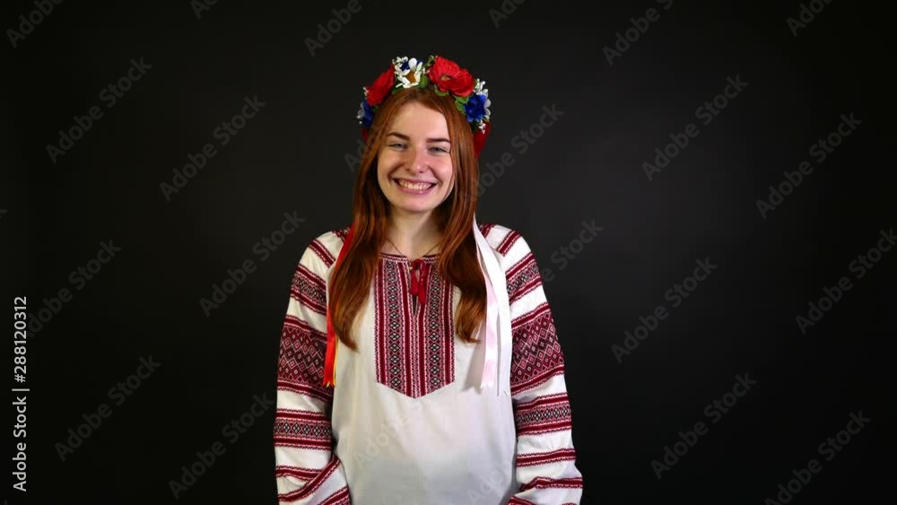 Red-haired girl in an embroidered shirt waving and smiling. Black background Red-haired girl in an embroidered shirt waving and smiling. Black background