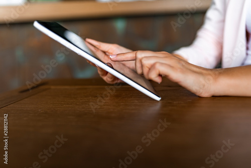 Close-up photo of female hands working with tablet computer. Woman using social network, texting and blogging. Young businesswoman using tablet computer in coffee shop