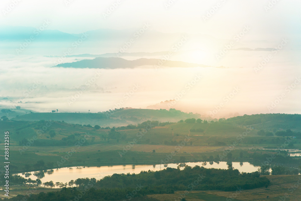 Mountain range with visible silhouettes through the morning colorful fog over pond water.