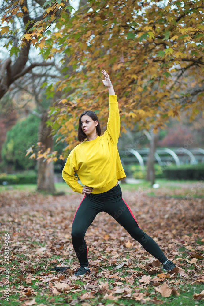 Female athlete stretching at city park in autumn. Sporty woman exercising outdoor.