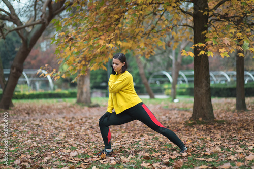 Female athlete stretching at city park in autumn. Sporty woman exercising outdoor.