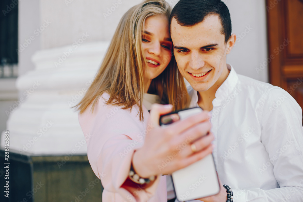 beautiful and stylish blonde along with her handsome guy standing near building in the summer city and use the phone in white case beautiful and stylish blonde along with her handsome guy standing near building in the summer city and use the phone in white case