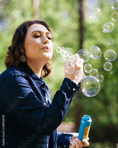 Careless young woman blowing soap bubbles outdoors