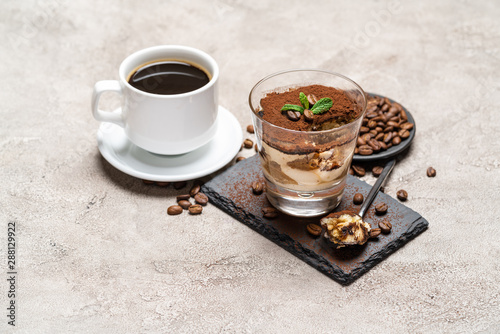 Portion of Classic tiramisu dessert in a glass cup on stone serving board and fres espresso coffee on concrete background photo