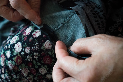 Macro elderly woman hands sewing on fabric, needle. Sew pants by old woman hand, seamstress at work with cloth fabric. Grandmother sews. Close up shot. Selective focus