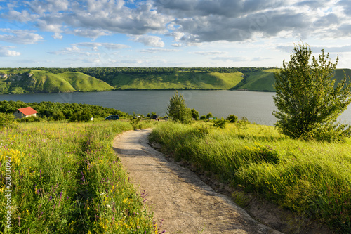 Scenic landscape of trail going through meadow with lush herbs and wildflowers down to river. Beautiful nature of Dniester river and Bakota area, part of the National Park 