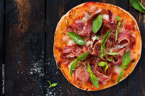 Homemade pizza with jamon, mozzarella and fresh basil leaves on an old wooden background. Top view.