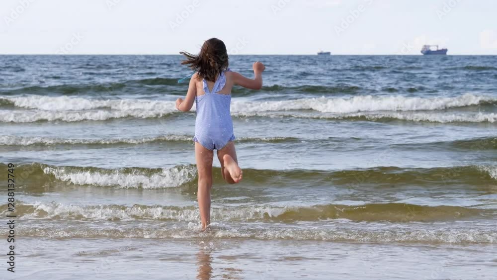 Little girl play in shallow Baltic sea water jump over tide waves having fun during summer vacation Little girl play in shallow Baltic sea water jump over tide waves having fun during summer vacation