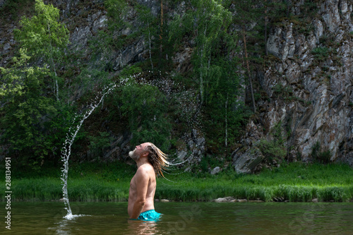 Model aged bearded man splashing water with his hair. Hair whip. .against a green summer background