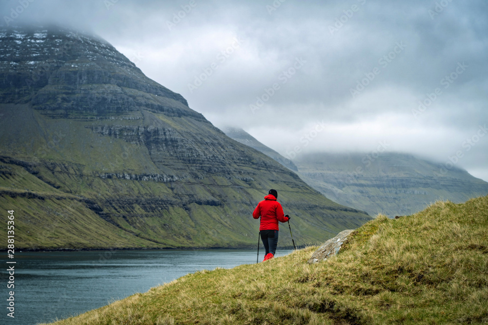 Young female hikers walking on a trail next to a wide fjord in Faroe Islands.