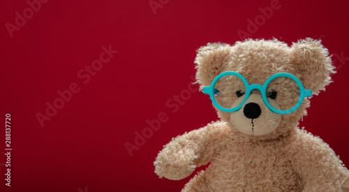 Cute teddy wearing eyeglasses against red background