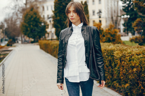 beautiful stylish young girl with long hair and a black leather jacket and glasses standing in the autumn city