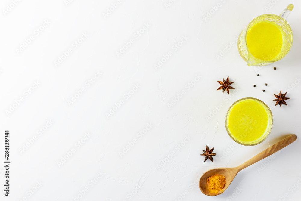 Golden milk from turmeric, vegetable milk, pepper, ginger, coconut oil, maple syrup in a glass on a white background. Traditional indian drink, copy space. Golden milk from turmeric, vegetable milk, pepper, ginger, coconut oil, maple syrup in a glass on a white background. Traditional indian drink, copy space.