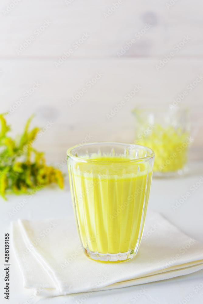 Golden milk from turmeric, vegetable milk, pepper, ginger, coconut oil, maple syrup in a glass on a white background. Traditional indian drink. Golden milk from turmeric, vegetable milk, pepper, ginger, coconut oil, maple syrup in a glass on a white background. Traditional indian drink.