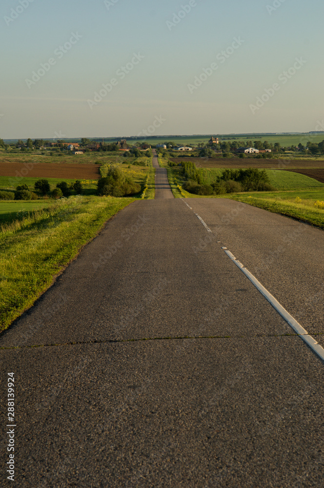 Naklejka premium old asphalt road through green fields at sunset
