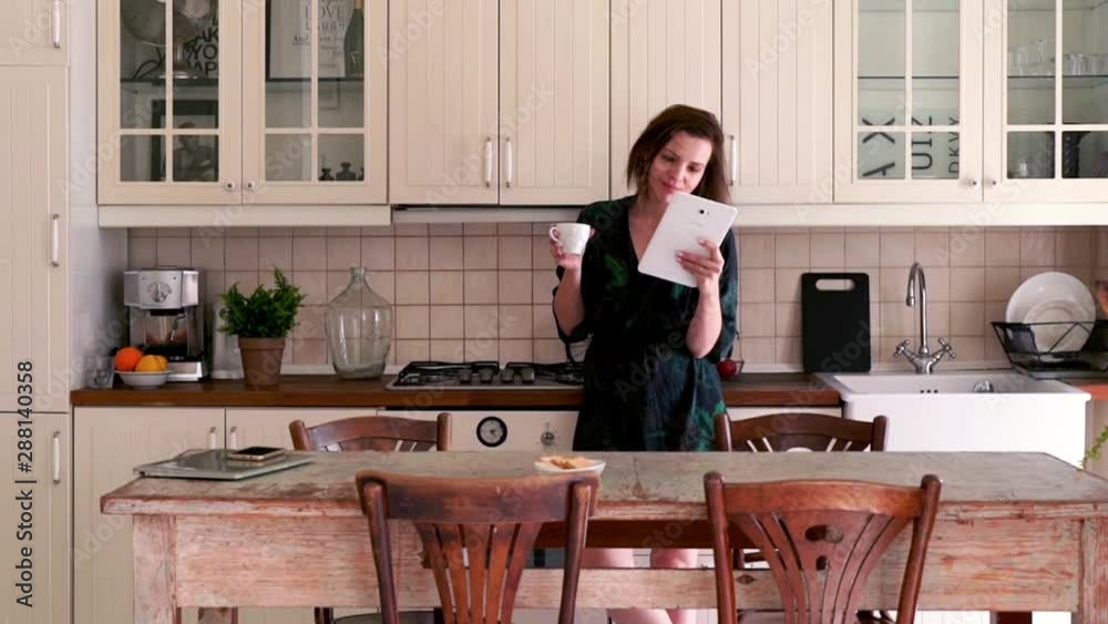Beautiful, young woman standing in bathrobe with tablet in the kitchen Beautiful, young woman standing in bathrobe with tablet in the kitchen