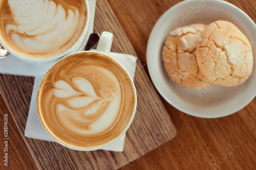 Cups of cappuccino coffee with cookies on wooden table