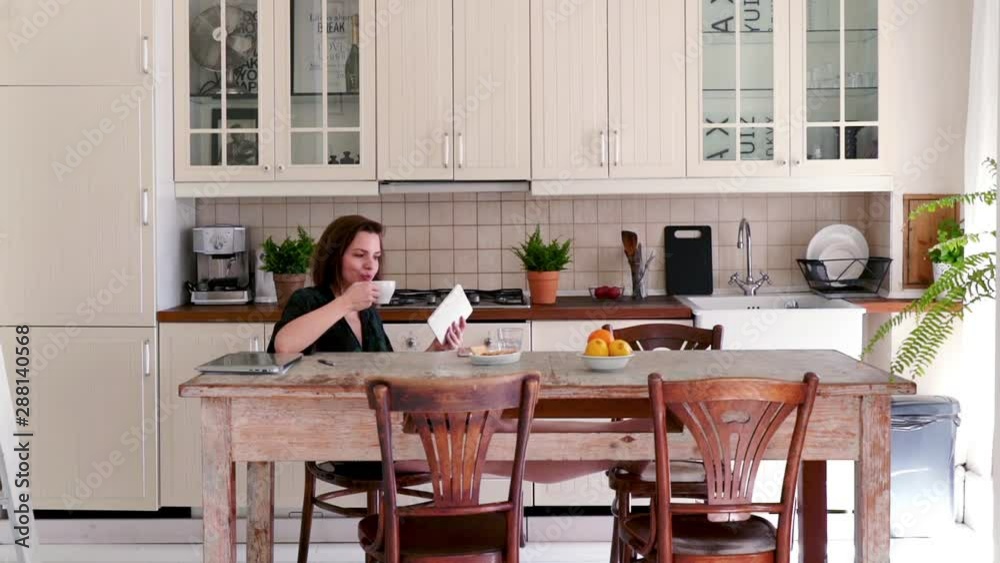 Beautiful, young woman sitting in bathrobe with tablet in the kitchen Beautiful, young woman sitting in bathrobe with tablet in the kitchen