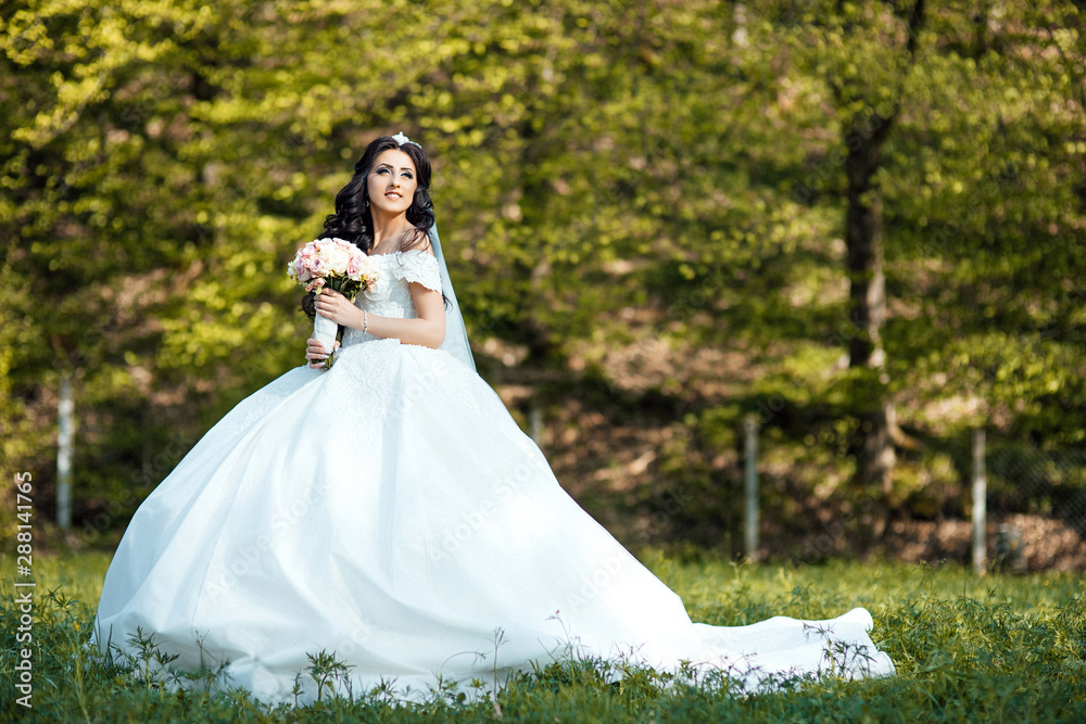 Happy bride in a beautiful dress walking in the park. Young beautiful stylish woman, bride, bridal fashion, spring trend, flowers, roses, hairstyle, beauty make-up, white dress. Wedding day. 