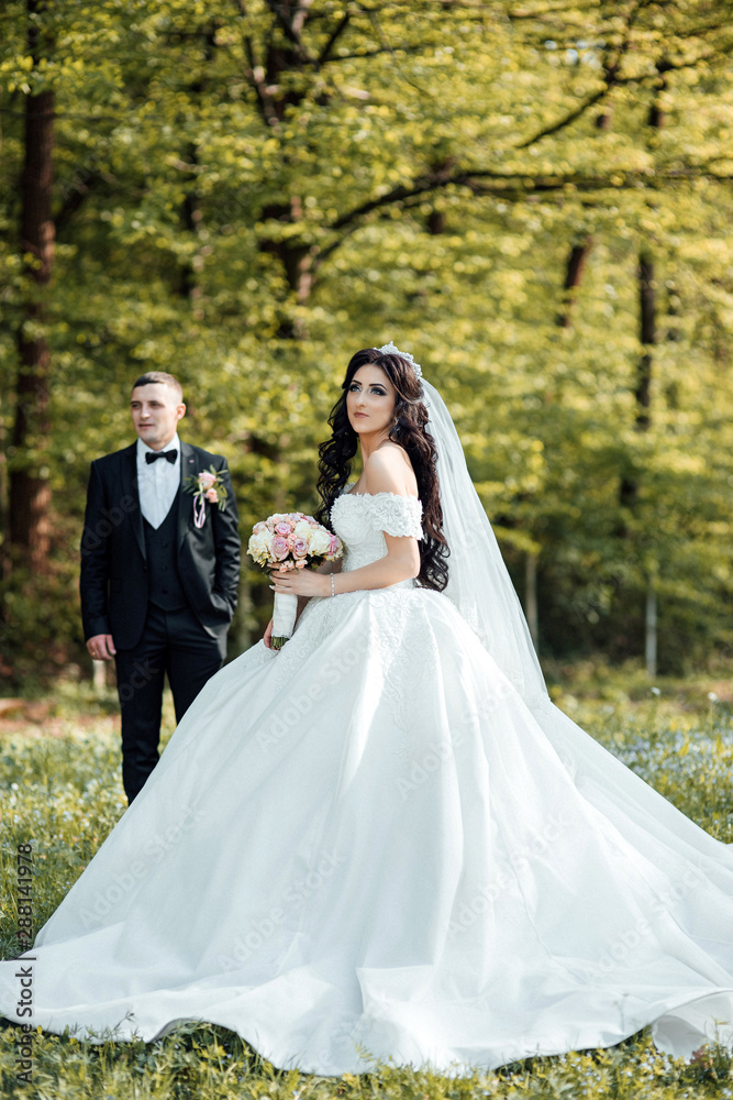 Newlywed couple with roses bouquet posing and kissing. Elegant bride and groom posing together outdoors on a wedding day.  Happy newlyweds posing in the park on their wedding day. 