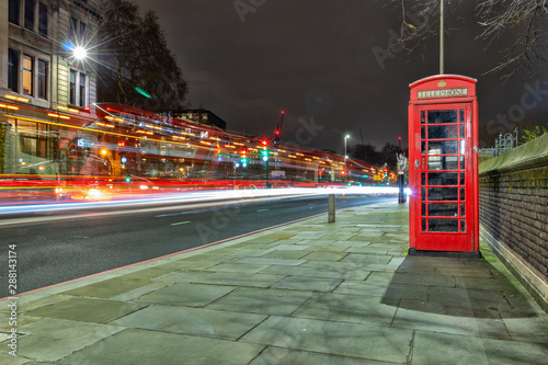 A red telephone box on a busy Lond street at night with light trails