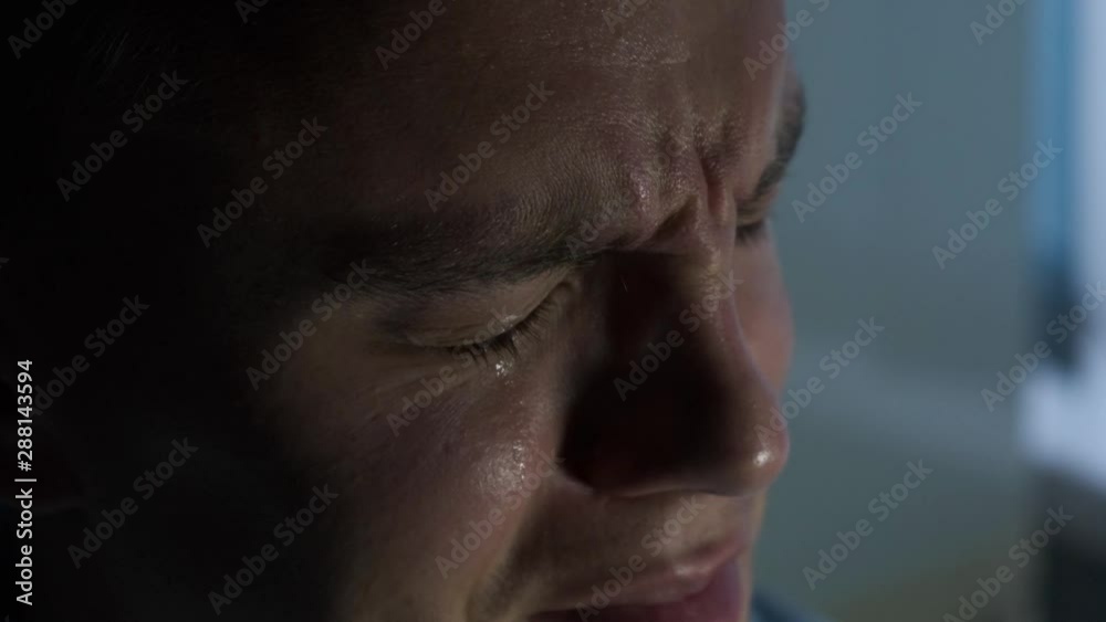 Unhappy man crying in a dark room, close up