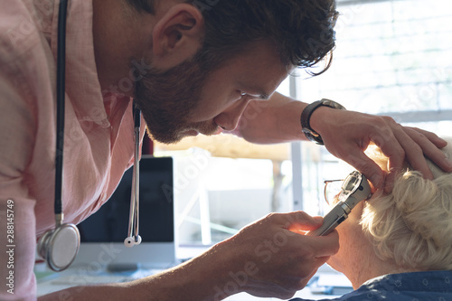 Male doctor checking senior female patient ear with otoscope photo