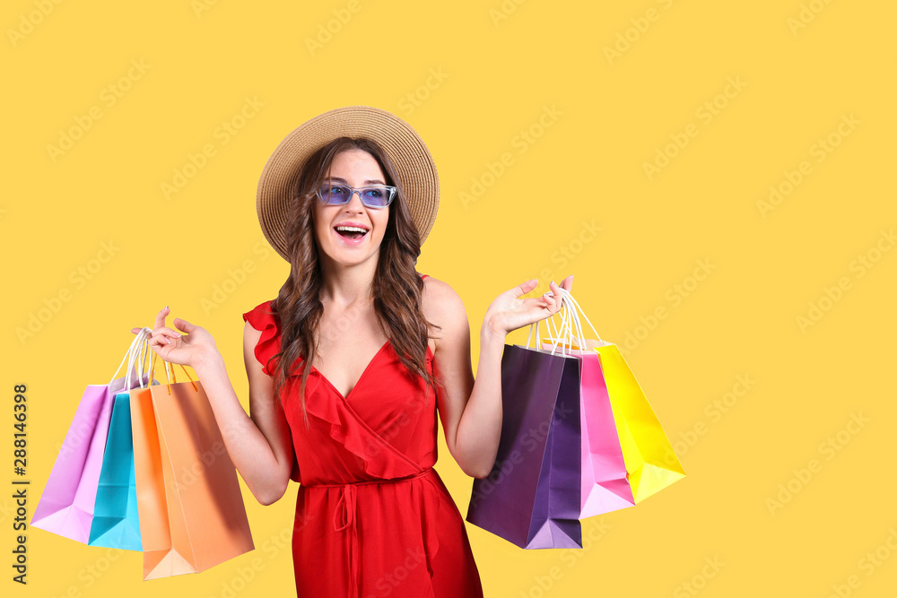 Black friday season sale concept. Attractive young woman with long brunette hair, wearing straw hat, holding many different blank shopping bags over yellow isolated background. Copy space, close up
