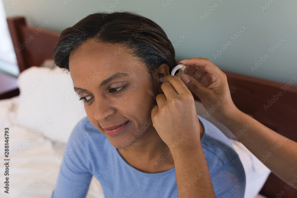 Senior woman fitting hearing aid by female doctor in bedroom at home Senior woman fitting hearing aid by female doctor in bedroom at home