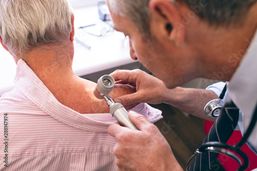 Male dermatologist examining senior patient through dermatoscopy