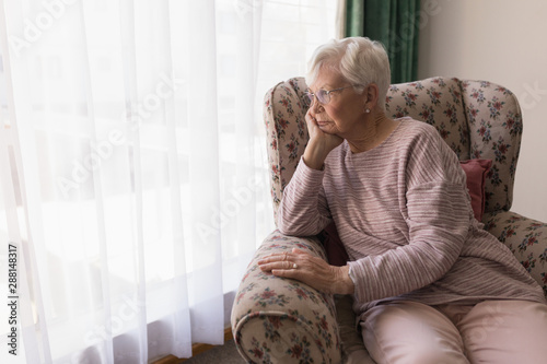 Front view of senior woman sitting on the couch and looking outside through window