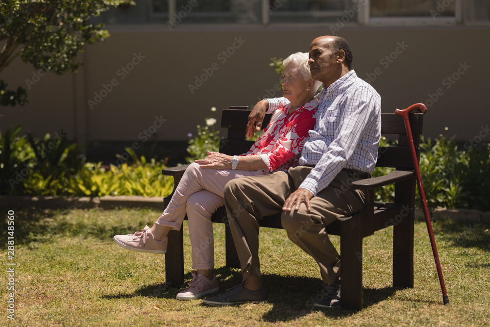 Obraz premium Side view of senior couple relaxing on bench in garden