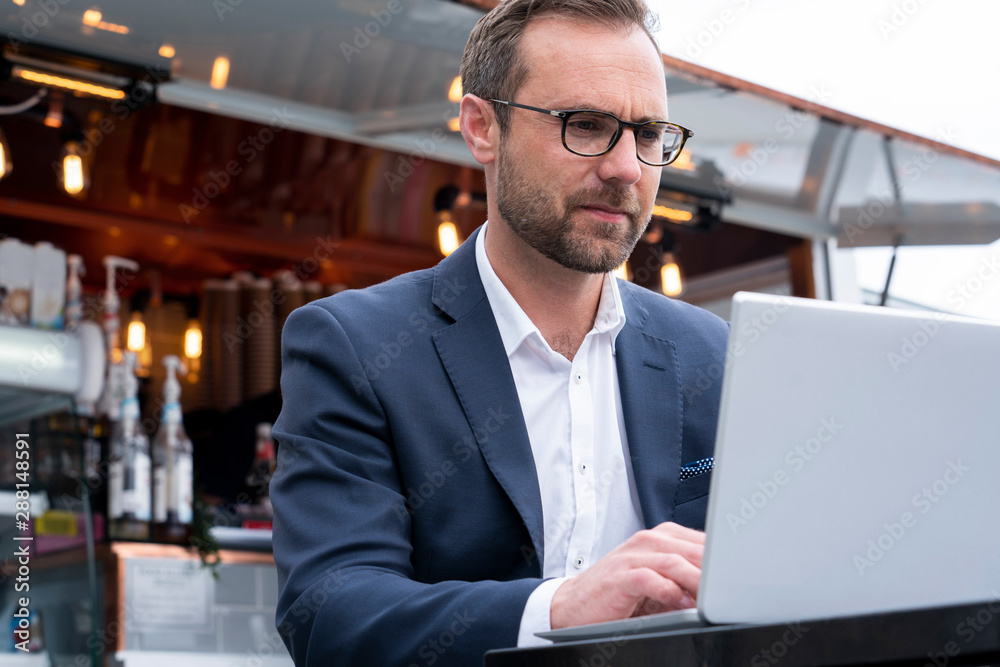 Mature Businessman Working On Laptop By Outdoor Coffee Shop