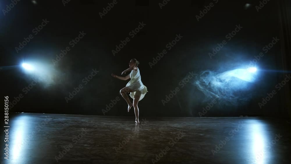 a girl in a white dress dances a modern ballet on the stage with smoke ...