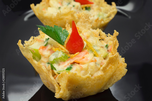 Parmesan cheese basket stufed with chicken salad and pout pepper in black background